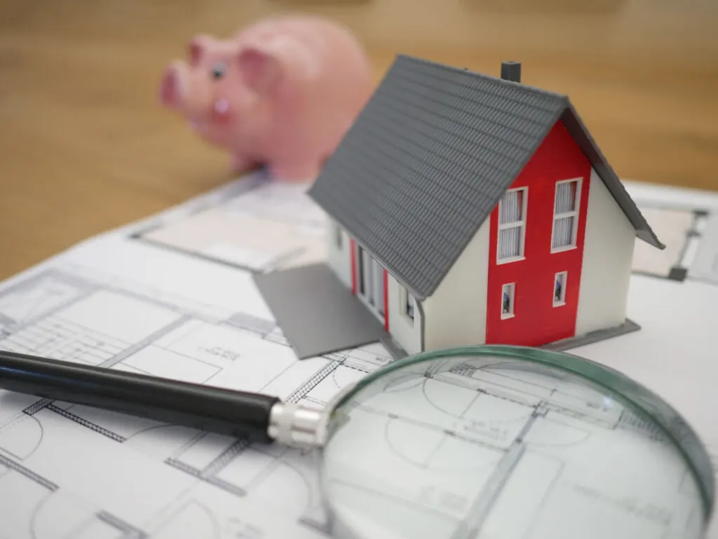 a house beside a magnifying glass and a piggy bank at the background